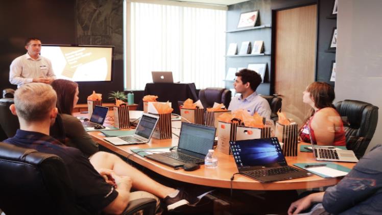 Maximizing The Impact Of Customer Data On Sales Velocity A sales manager discussing sales velocity with a team sitting at a conference table with laptops.